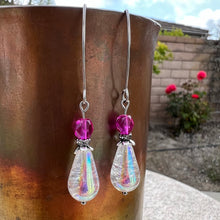 Bernd Offerings continues their 'Musical' theme with earrings inspired by My Fair Lady!  These stunning earrings showcase a large Czech glass crackle crystal teardrop with an exquisite aurora borealis finish complemented by a beautiful Czech glass faceted fire polished round in a vibrant violet fuchsia. A wavy Czech glass rhinestone gunmetal spacer and antique silver flower bead cap along with comfortable stainless steel V-shaped Marquise ear wires complete the design.