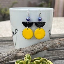 These beautiful geometric earrings feature a double-sided copper circle and semi-circle with an oil drip enamel finish in yellow and black. A cobalt blue faceted crystal rondelle with an aurora borealis finish completes the look. Earrings measure approximately 2" long on stainless steel ear wires with silicone backs.