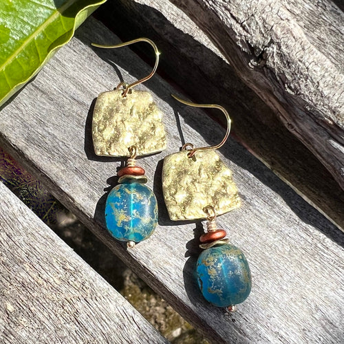 These gorgeous earrings showcase a chunky matte Caribbean blue Czech glass nugget with a unique Picasso finish, suspended from a hammered raw brass trapezoid that reflects the light at every turn. A matte metallic antique copper Czech glass rondelle and wavy brass spacer add warmth and texture while detailed wire wrapping completes the design. Earrings measure approximately 2 1/4