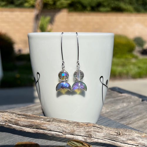 Shine like a star and add a touch of elegance to any outfit with these celestial-inspired earrings that reflect the light with every turn. They feature a stunning electroplated AB glass crescent paired with a 10mm iridescent multi-faceted AB glass round. A square hammered rhodium spacer adds the perfect complement, while comfortable V-shaped marquise ear wires complete the design.

Earrings measure just under 2