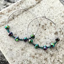These stunning hoop earrings feature faceted glass rondelles with an iridescent violet and green Aurora Borealis finish, paired with delicate Toho seed beads in a metallic green finish with subtle blue and violet undertones.

Set on 30 mm stainless steel hoops (approximately 1.18”), these shifty beauties are lightweight, comfortable, and look amazing with everything from jeans to dresses. They also make a thoughtful gift for someone special.